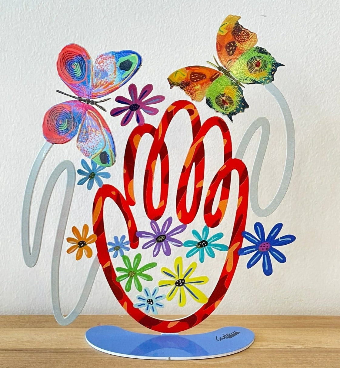 Hamsa is an ancient talisman known as protection against the evil eye and a virtue for happiness, wealth and health This special Hamsa is decorated with butterflies and flowers in vibrant colors. The Hamsa is painted on both sides, and comes with a base so you can place it anywhere you want. Gerstein's signature is printed on the base.
